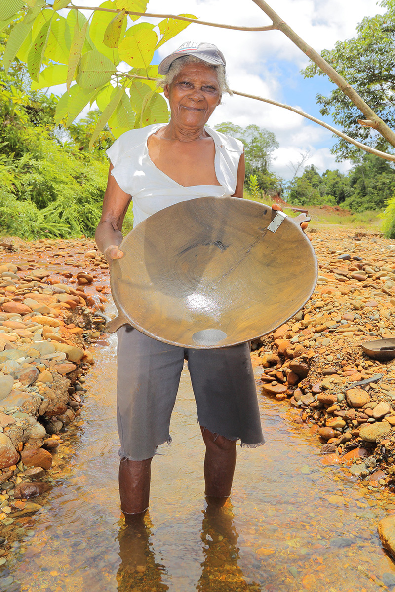 Woman gold miner standing in a stream holding a round, wooden panning bowl used for panning gold.