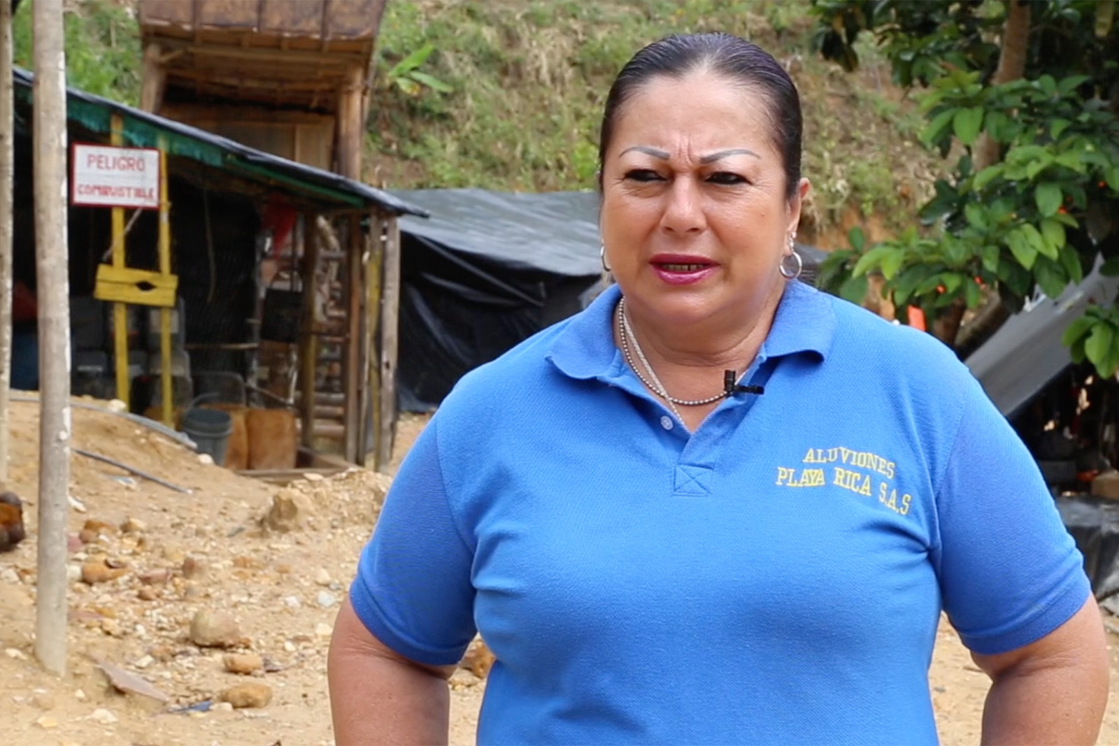 Woman gold miner in blue uniform standing in front of mining equipment in a mining area on a rocky shore in a rainforest in Antioquía, Colombia.